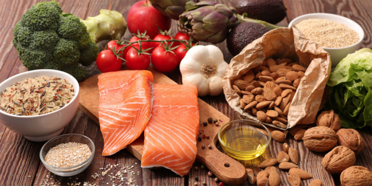 На столі лежать корисні продукти: червона риба, овочі, оливкова олія, горіхи, крупа