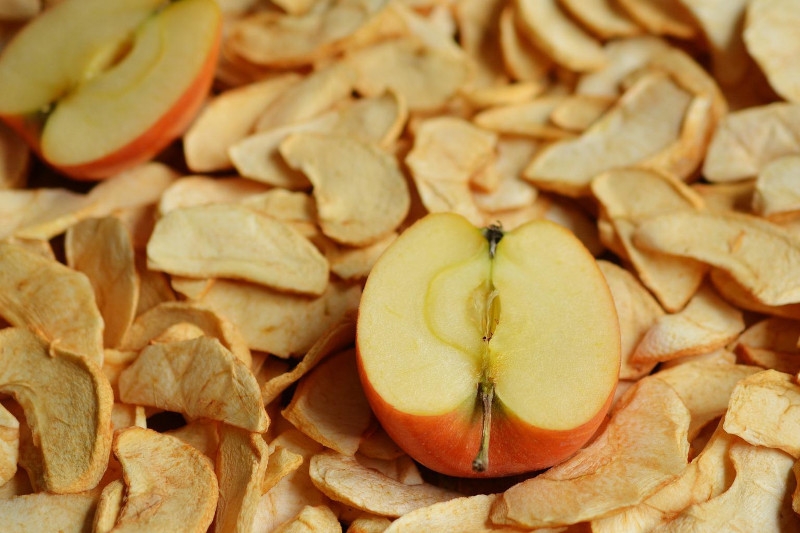 На фото половина свіжого яблука, яке лежить на сушених чипсах з яблук
