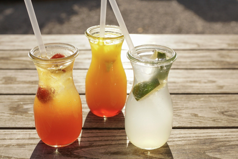 На столі розміщено три стакани в яких налили різні свіжовичавлені соки, лайм, полуниця, апельсин.